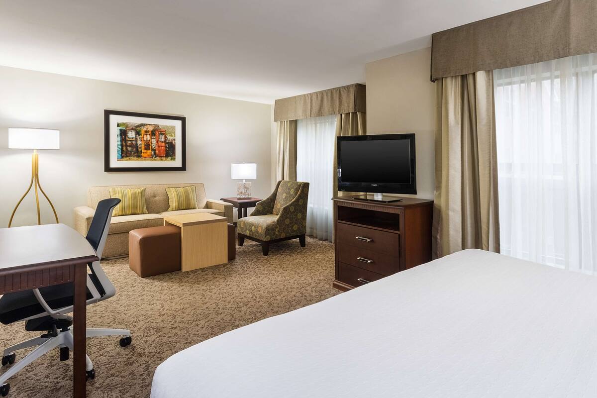 A hotel room with a large bed, a desk with a chair, a sofa, a TV, and a framed picture on the wall.