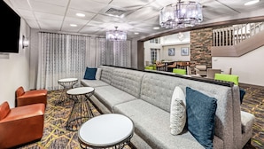 A modern hotel lobby with a grey sofa, round tables, and a staircase.