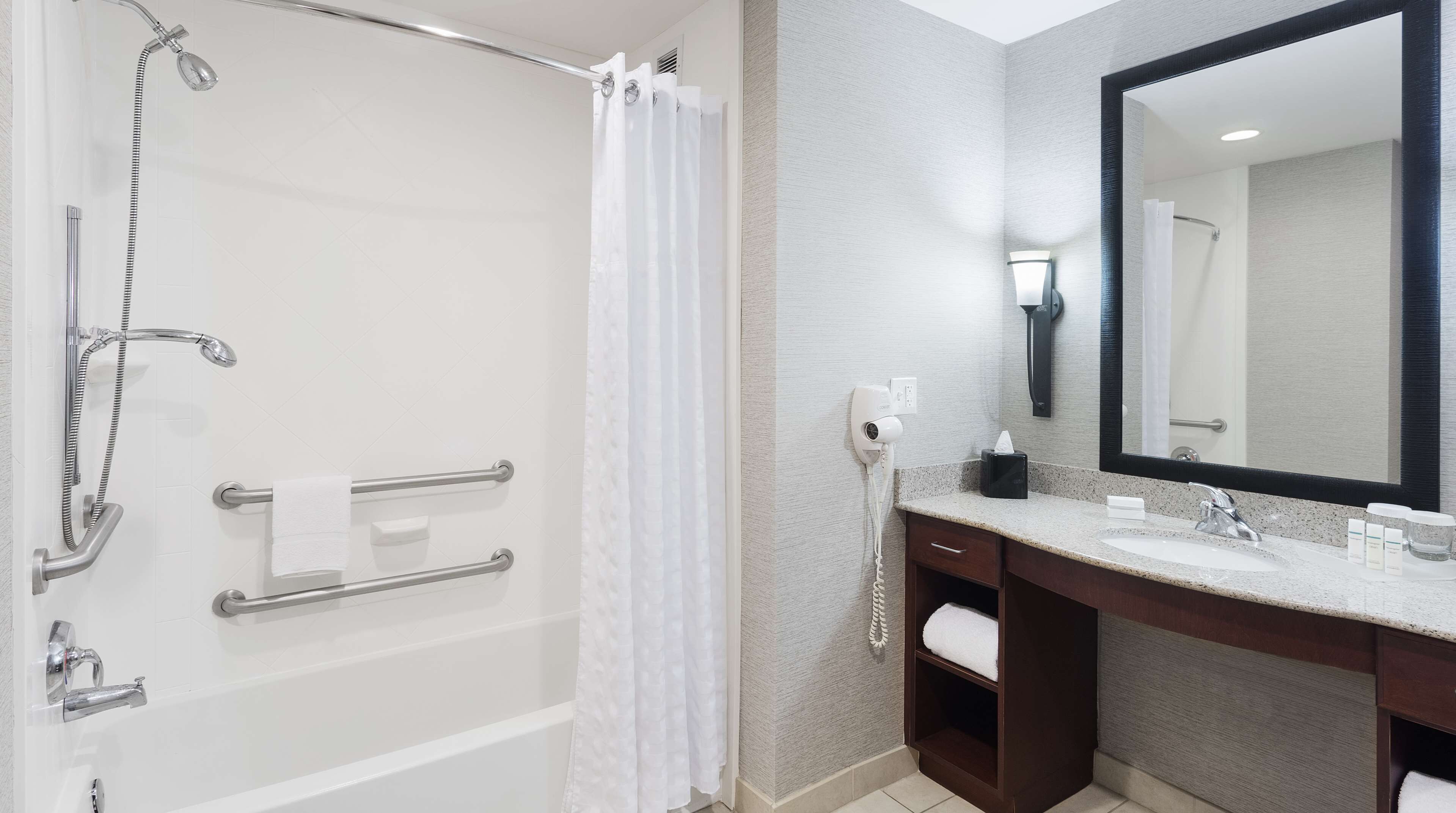 Un baño moderno con cabina de ducha, barras de apoyo, tocador con lavabo y un espejo grande.