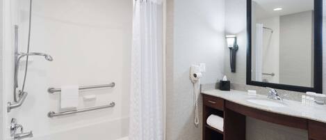 Un baño moderno con cabina de ducha, barras de apoyo, tocador con lavabo y un espejo grande.