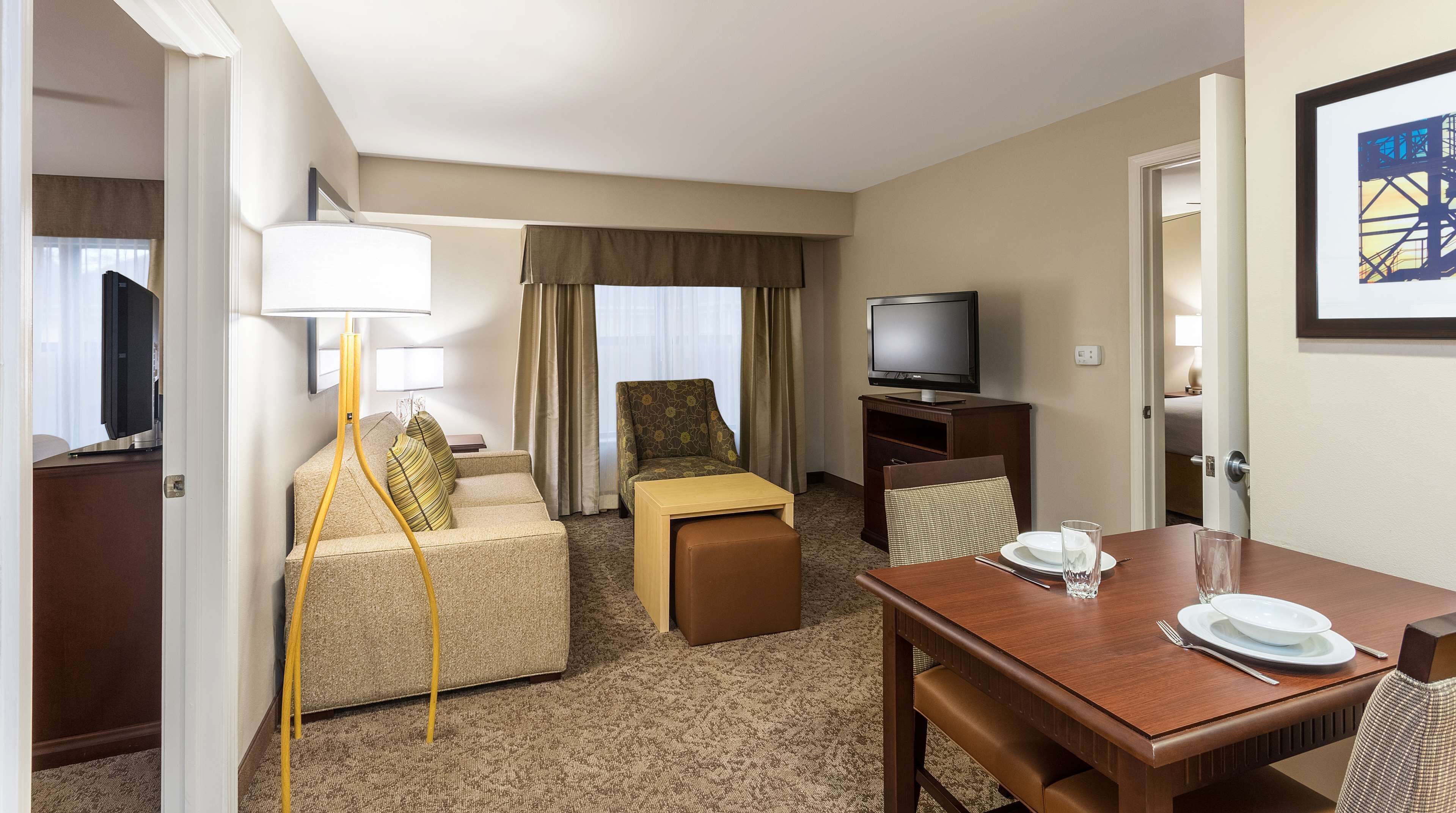 A hotel room with a sofa, a small table, a television, and a dining area with a table set for two.