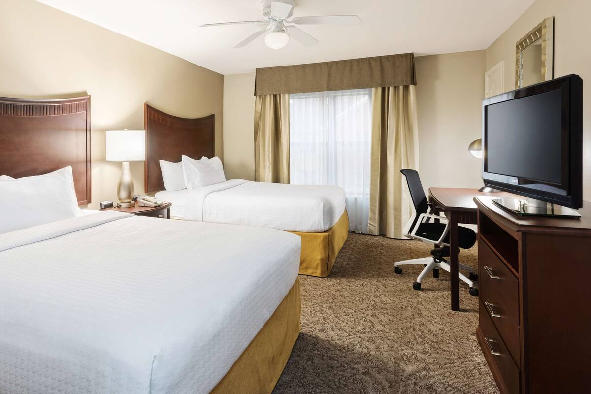 A hotel room with two beds, a TV, a desk with a chair, and a ceiling fan.