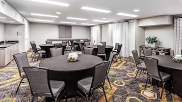 Une salle de conférence équipée de tables et de chaises rondes, d’un coin cuisine et d’un tapis à motifs.