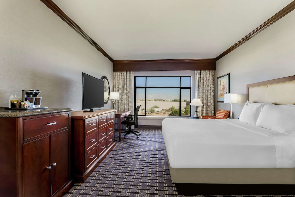 A hotel room with a large bed, a desk with a chair, a television, and a window with a view of the desert.
