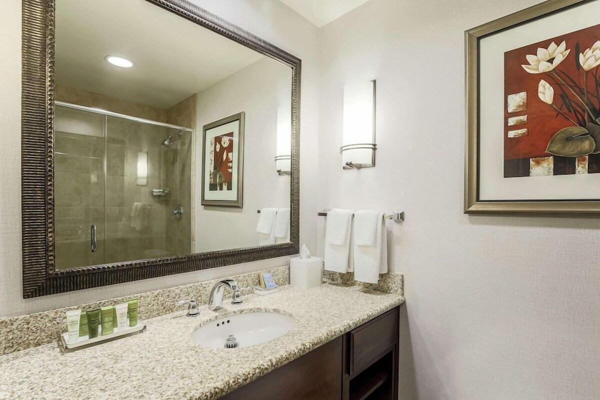 A bathroom with a large mirror, a sink, and a framed artwork on the wall.