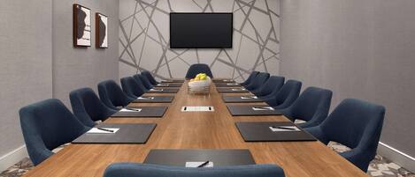 A conference room with a long table, blue chairs, a flat-screen TV, and a patterned wall.