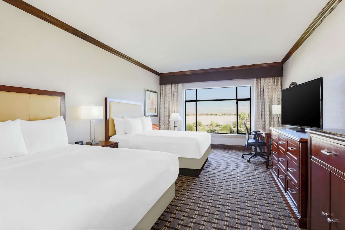A hotel room with two beds, a desk, a television, and a large window with a view.