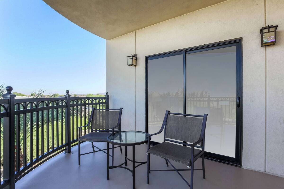 A balcony with two chairs and a glass table, a sliding glass door, and a small wall-mounted light fixture.