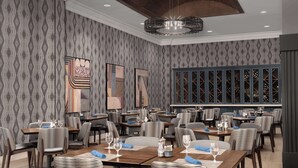 A dining area with patterned wallpaper, modern chairs, and tables set with wine glasses and napkins. - Hilton Phoenix Chandler (Chandler)