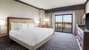 A hotel room with a large bed, a TV, a dresser, a nightstand, a lamp, and a balcony with a view. - Hilton Phoenix Chandler (Chandler)