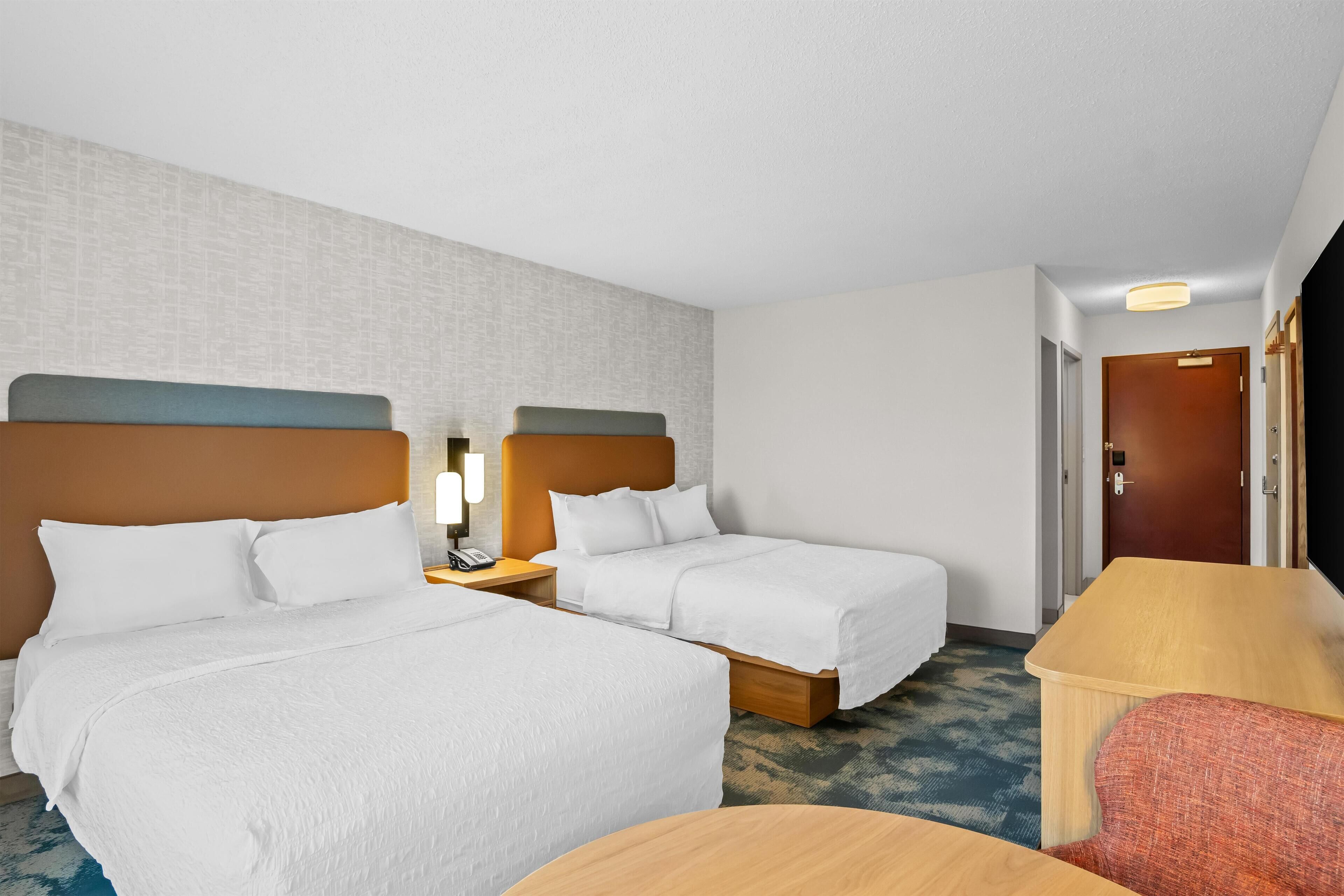 A hotel room with two beds, a desk, a chair, and a door.