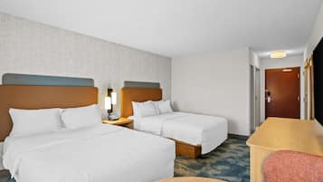 A hotel room with two beds, a desk, a chair, and a door.