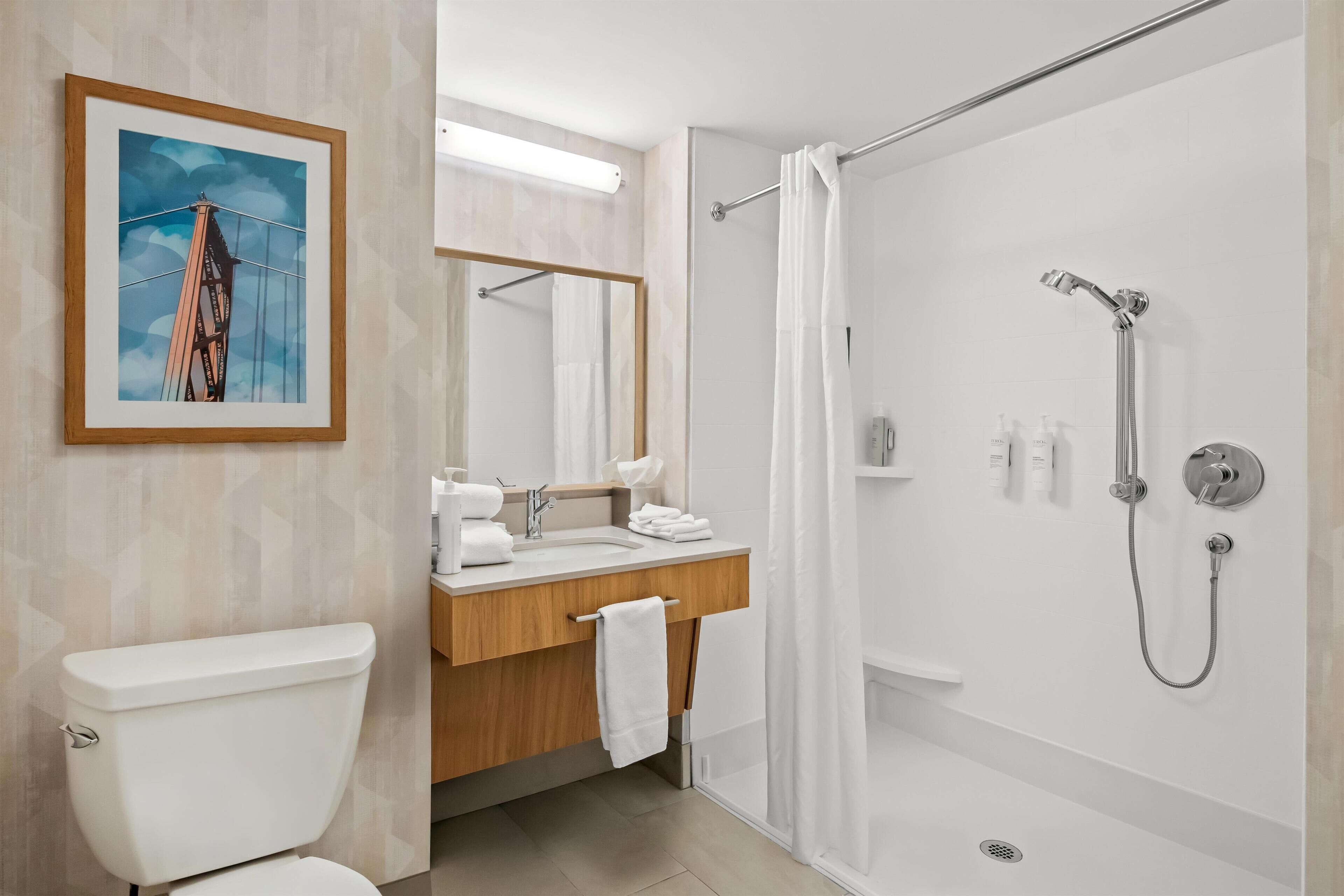 Un baño moderno con inodoro, lavamanos, espejo, ducha y un cuadro en la pared.