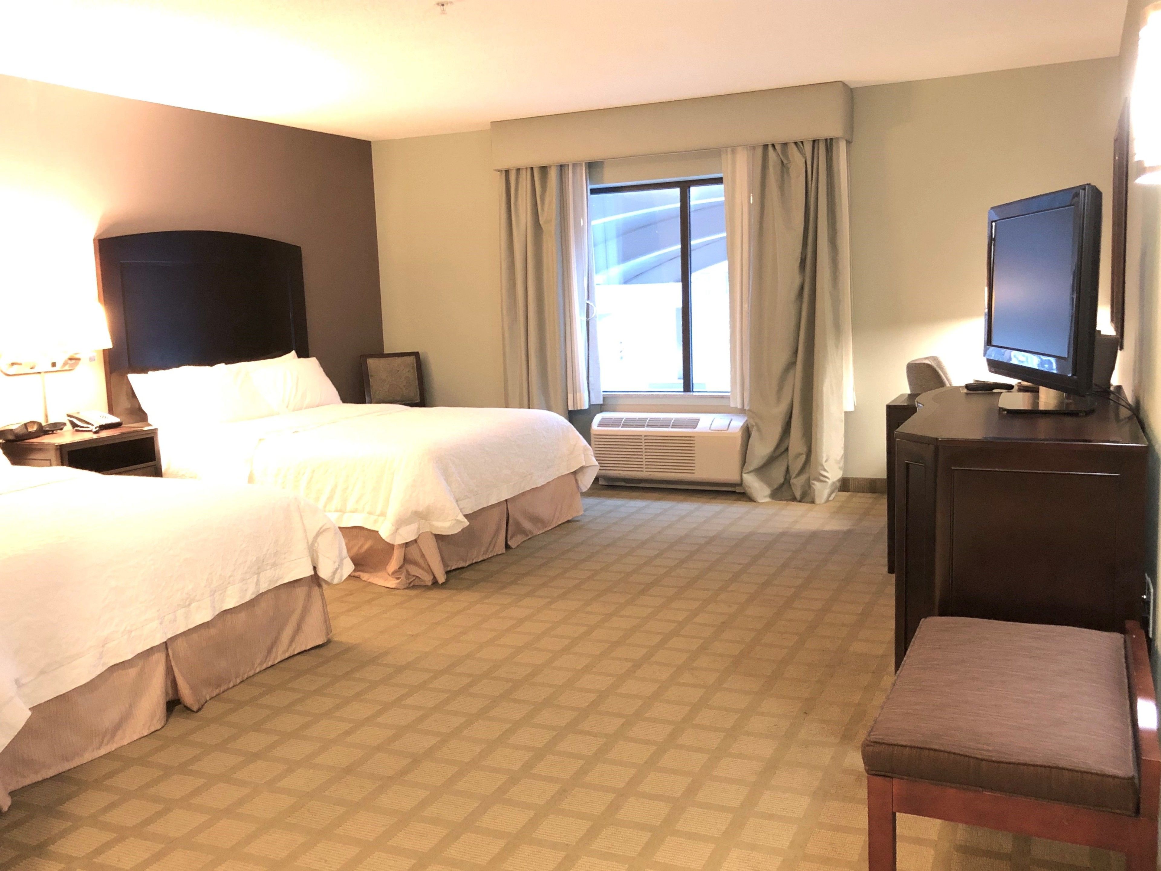 Een hotelkamer met twee bedden, een televisie, een bureau en een raam met gordijnen.
