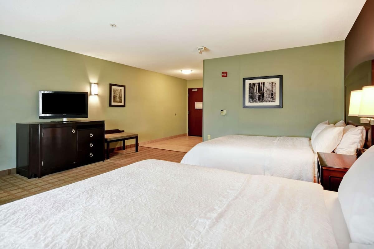 A hotel room with two beds, a TV, a desk, and a door.