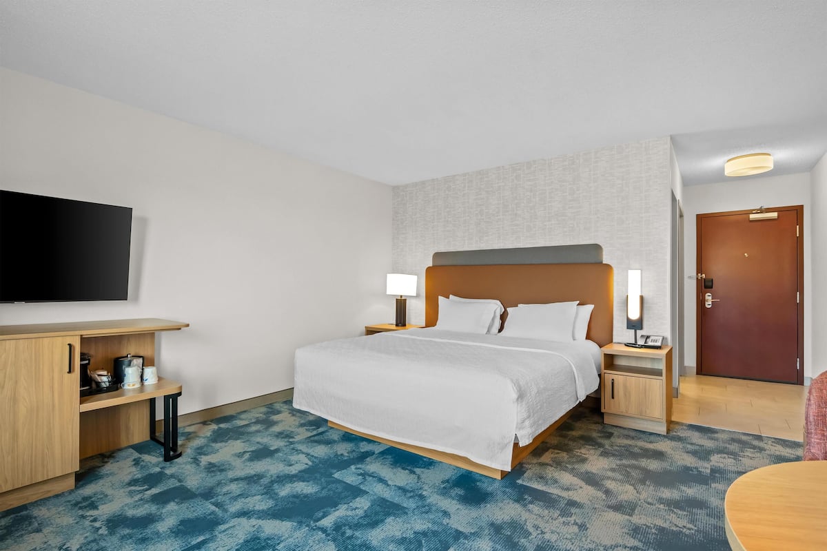 A hotel room with a bed, bedside tables, a TV, and a desk with a chair.