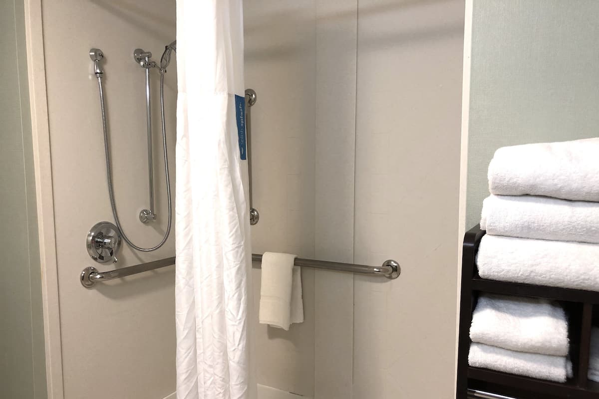 A bathroom with a shower, a towel rack with folded towels, and a white curtain.