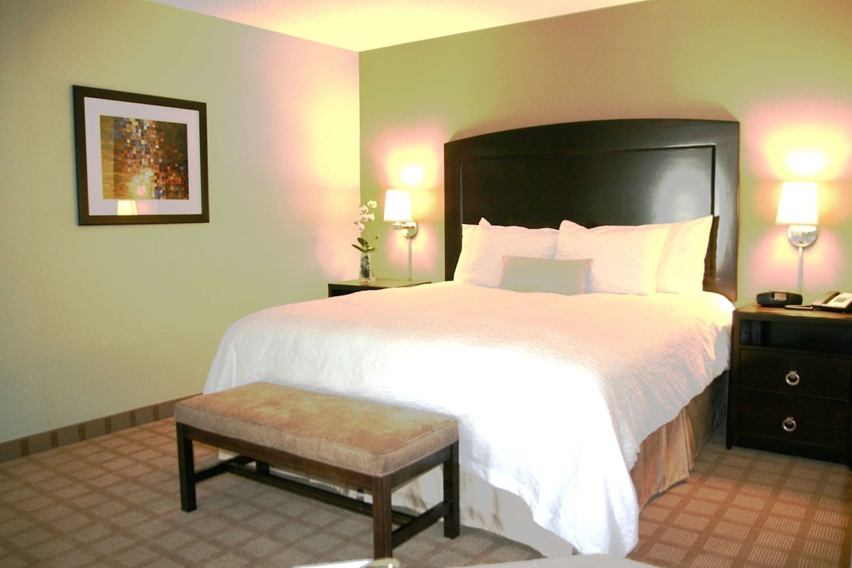 A neatly arranged hotel room with a bed, bedside tables, a bench, and a framed picture on the wall.