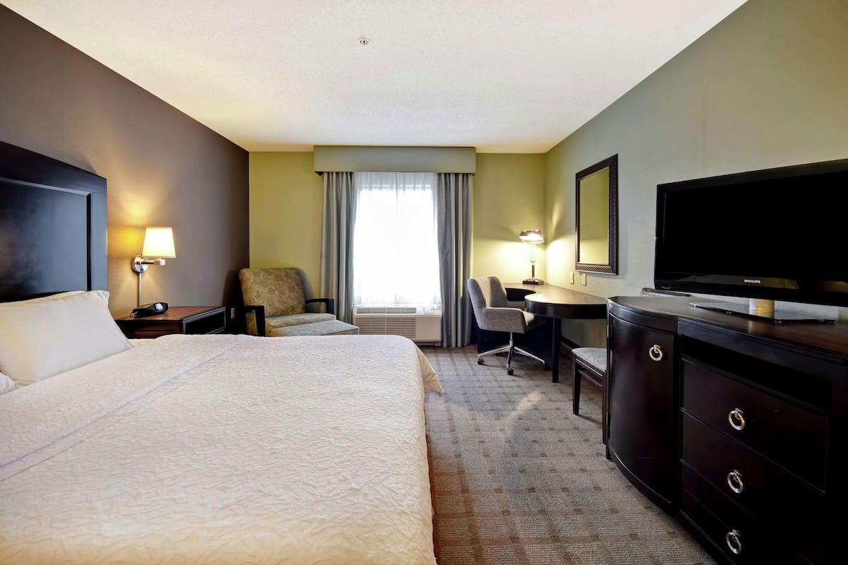 A hotel room with a large bed, a desk, a chair, a television, and a dresser.