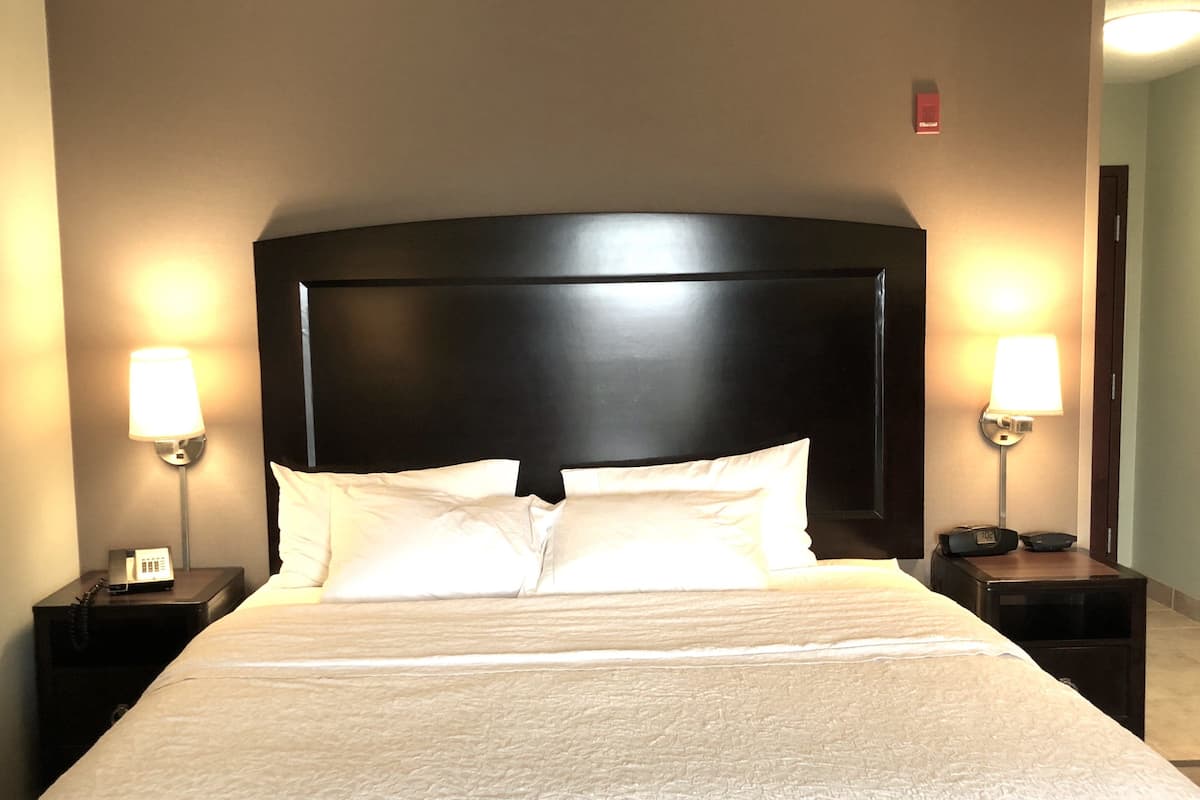A hotel room with a large bed, two bedside tables, and two wall-mounted lamps.