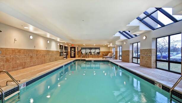An indoor swimming pool with clear water, a sunroof, and a seating area with tables and chairs. - Hampton Inn & Suites Detroit-Canton (Canton)