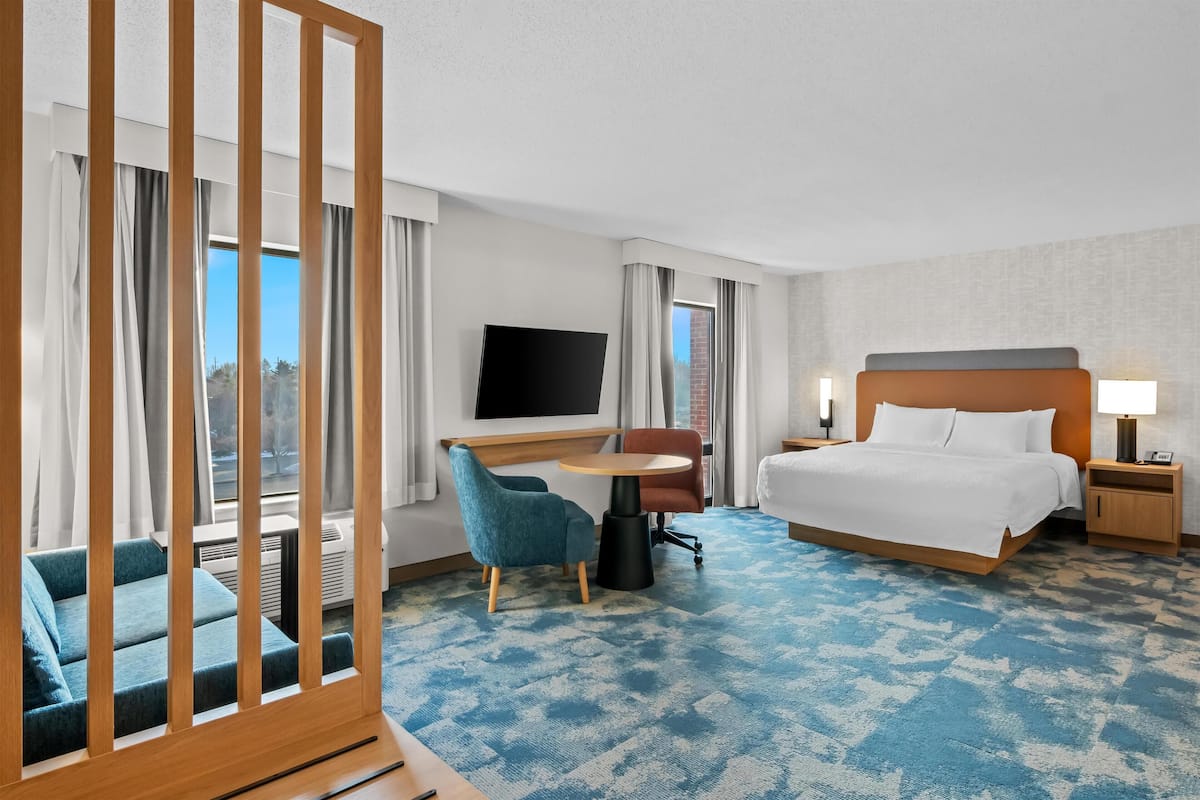 A hotel room with a bed, a desk, a TV, a chair, and a view of the outdoors.
