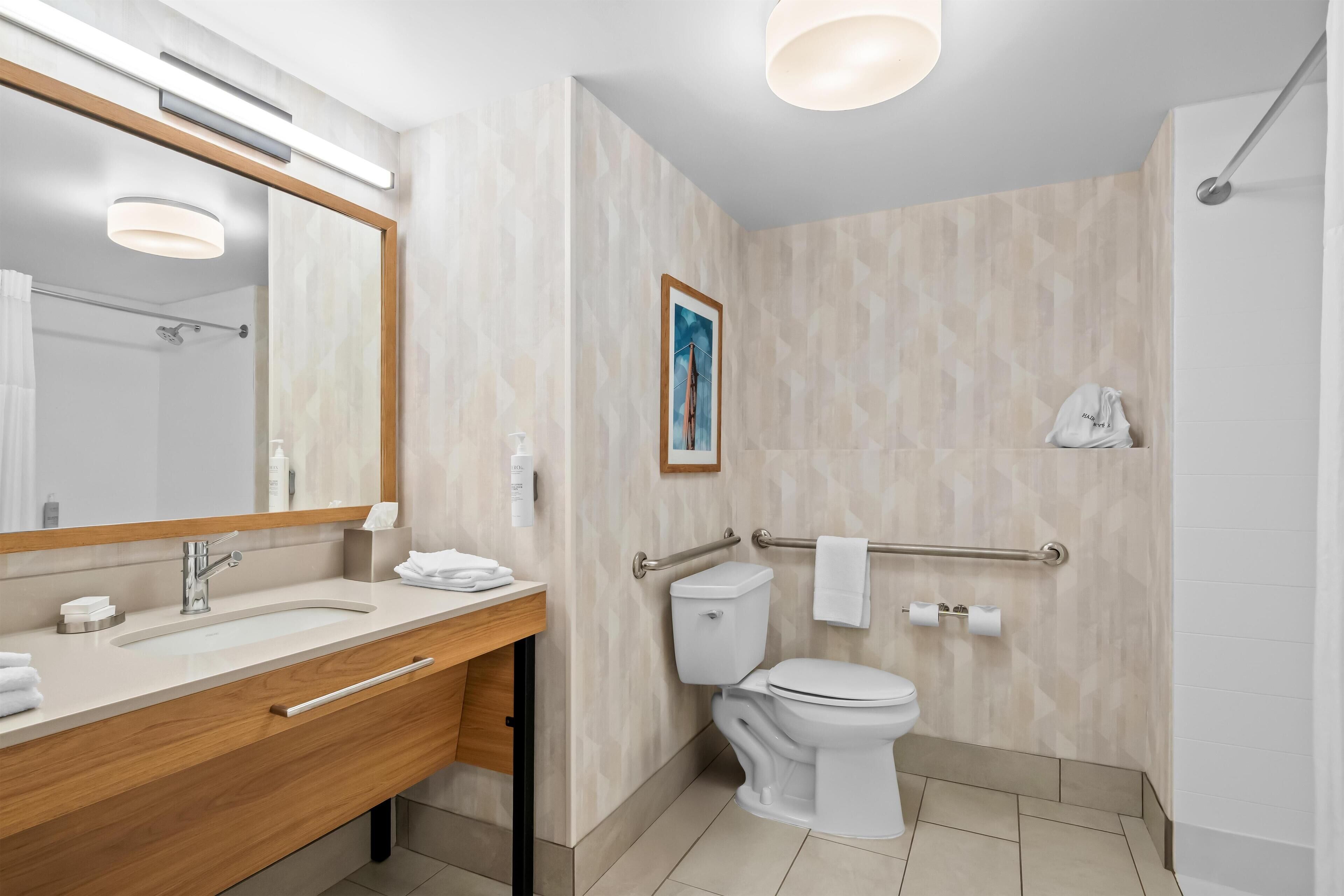 A modern bathroom with a wooden vanity, a large mirror, a toilet with a grab bar, and a shower area.