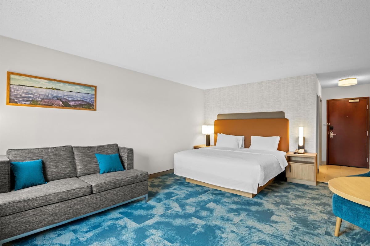 A hotel room with a bed, a sofa, a small table, and a painting on the wall.