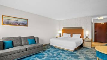 A hotel room with a bed, a sofa, a small table, and a painting on the wall.