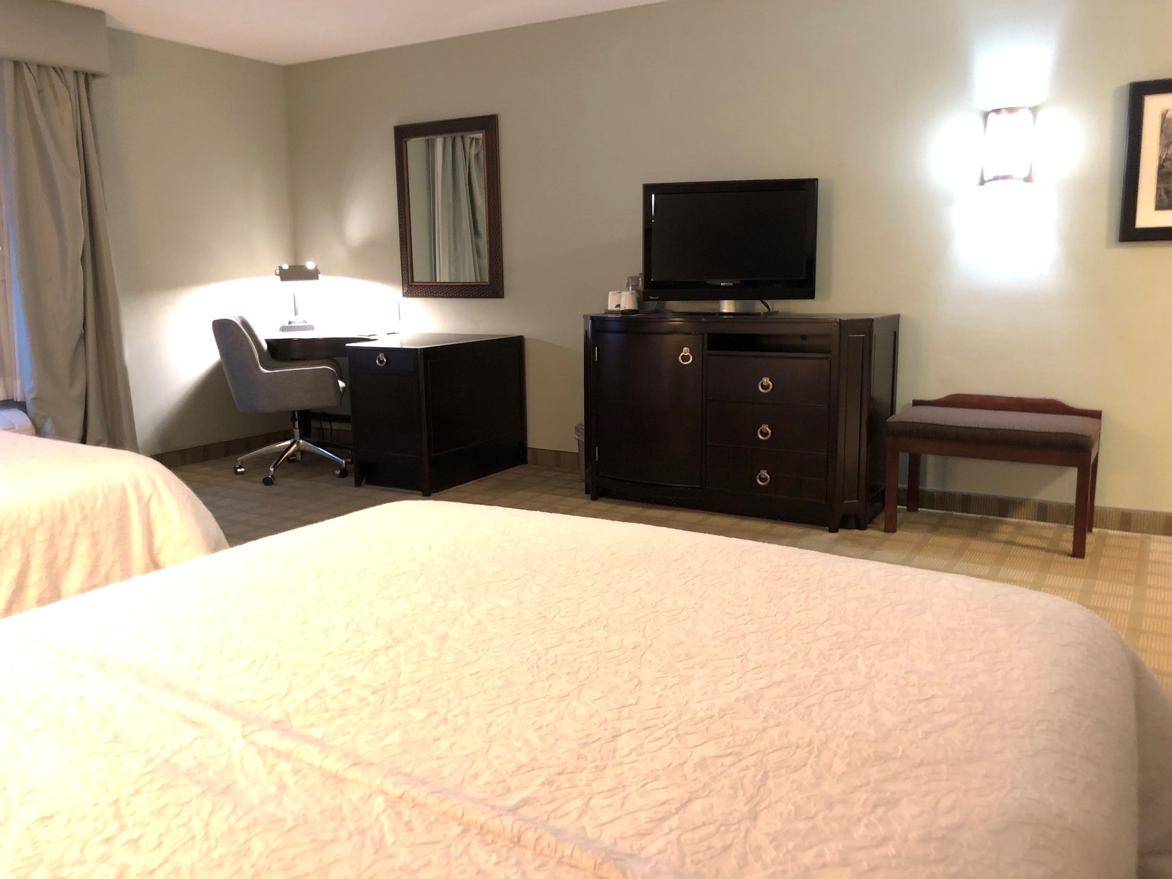 A hotel room with two beds, a desk, a television, and a chair.