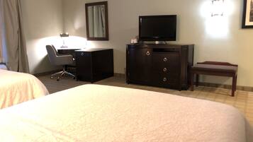 A hotel room with two beds, a desk, a television, and a chair.