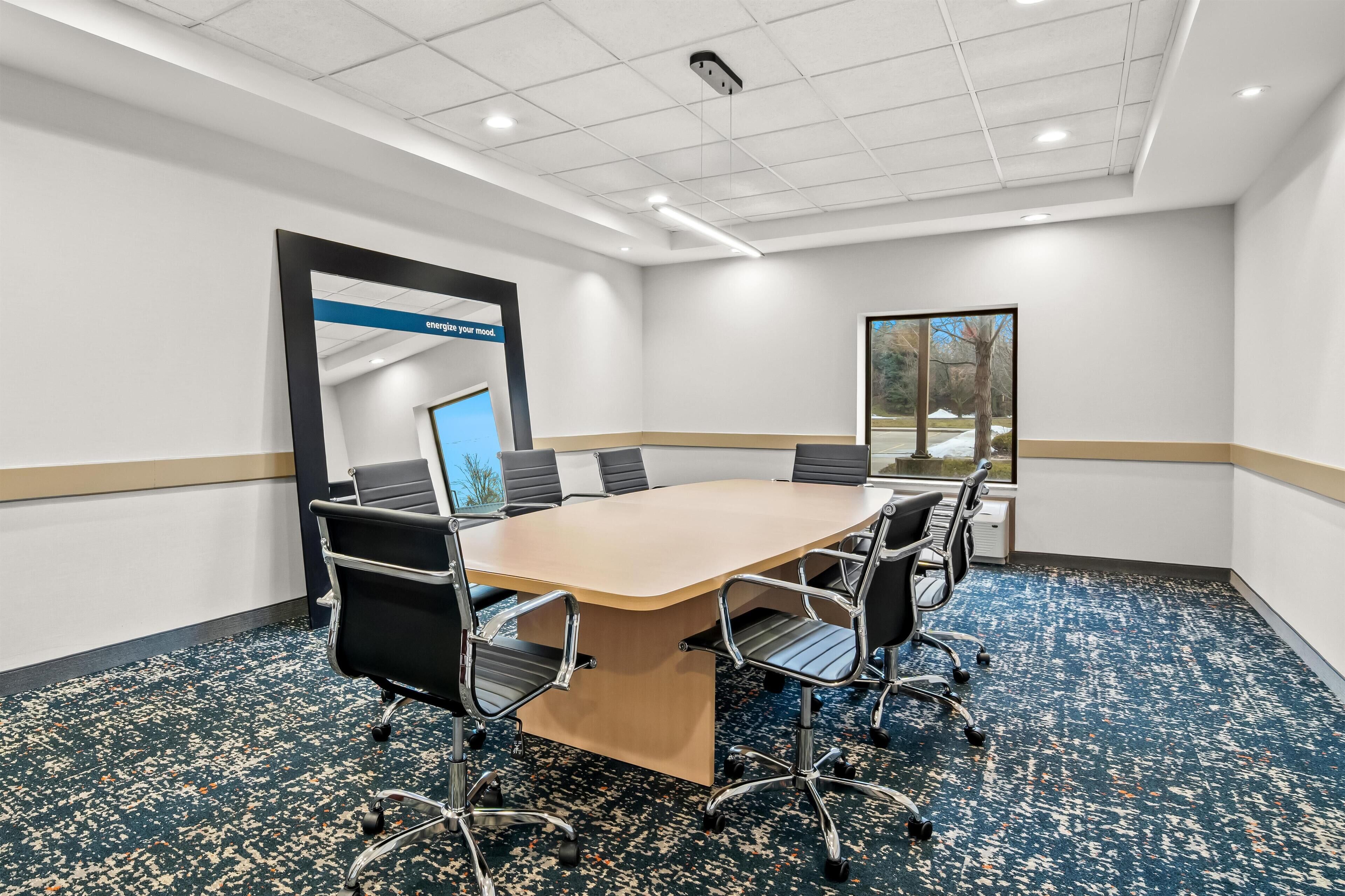 A conference room with a large table, six chairs, and a carpeted floor.