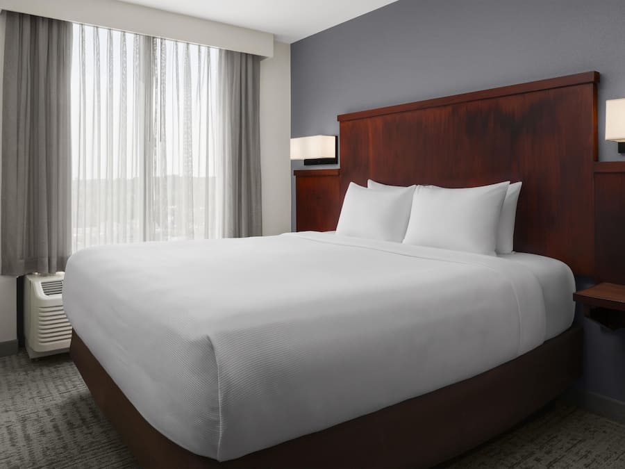 Une chambre d’hôtel avec un grand lit, une fenêtre avec des rideaux, une lampe fixée au mur et un radiateur.