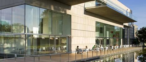 A modern building with a glass facade and a reflective water feature in front.