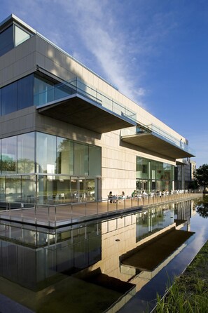 Un bâtiment moderne doté d’une façade en verre et agrémenté d’un élément décoratif aquatique réfléchissant à l’avant.