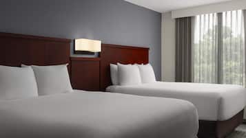 Een hotelkamer met twee bedden, een nachtkastje, een wandlamp en een raam met gordijnen.
