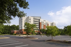 Un hôtel moderne à la façade en briques, avec plusieurs étages et un parking doté d’emplacements délimités.