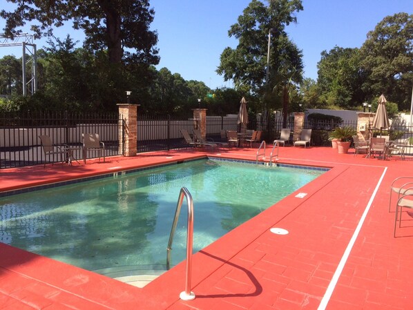 A swimming pool with a red deck, surrounded by lounge chairs and umbrellas, with trees in the background.