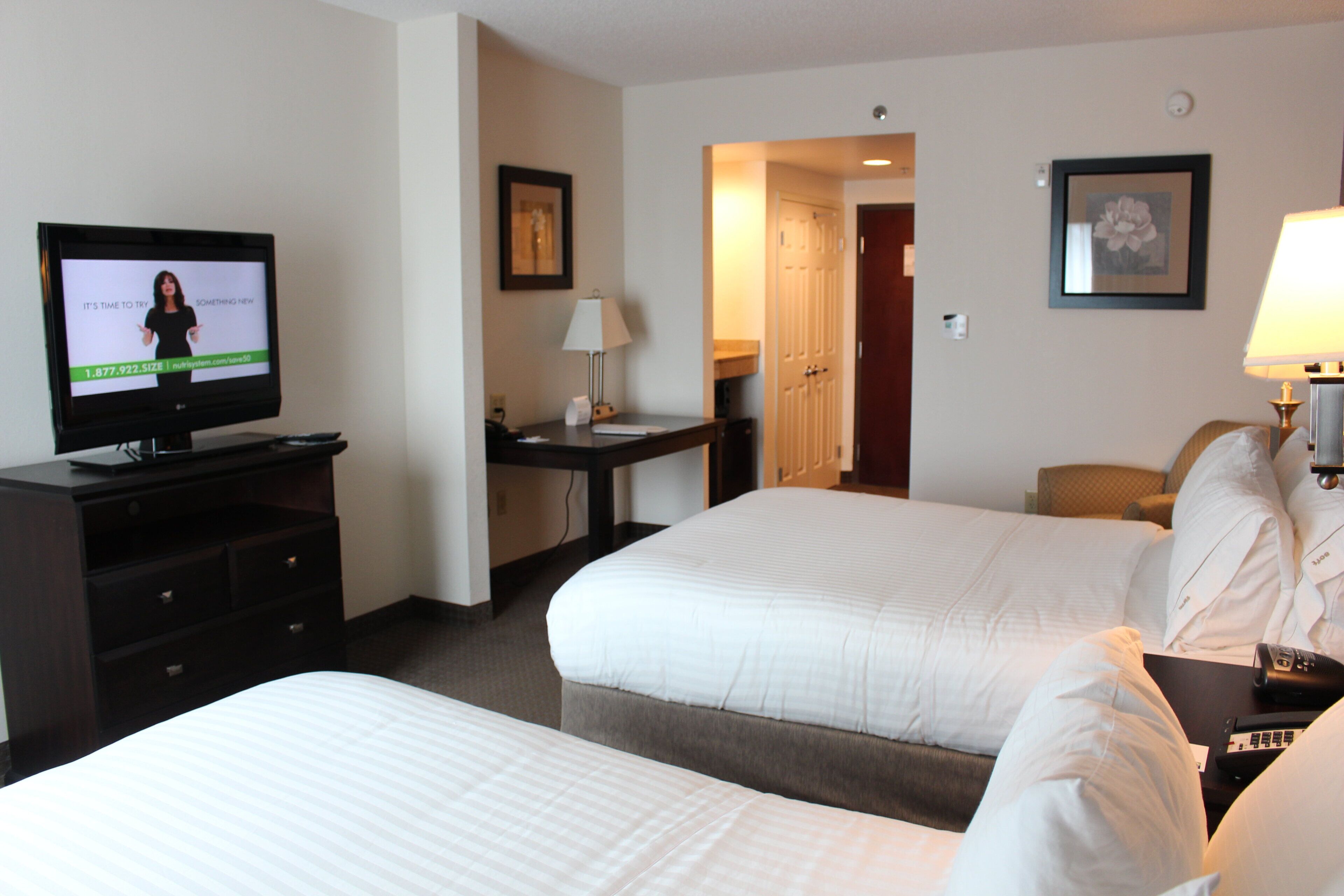 A hotel room with two beds, a desk with a computer, a television, and a lamp.