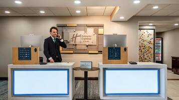 A hotel reception desk with two receptionists, a Holiday Inn Express sign, and a vending machine.