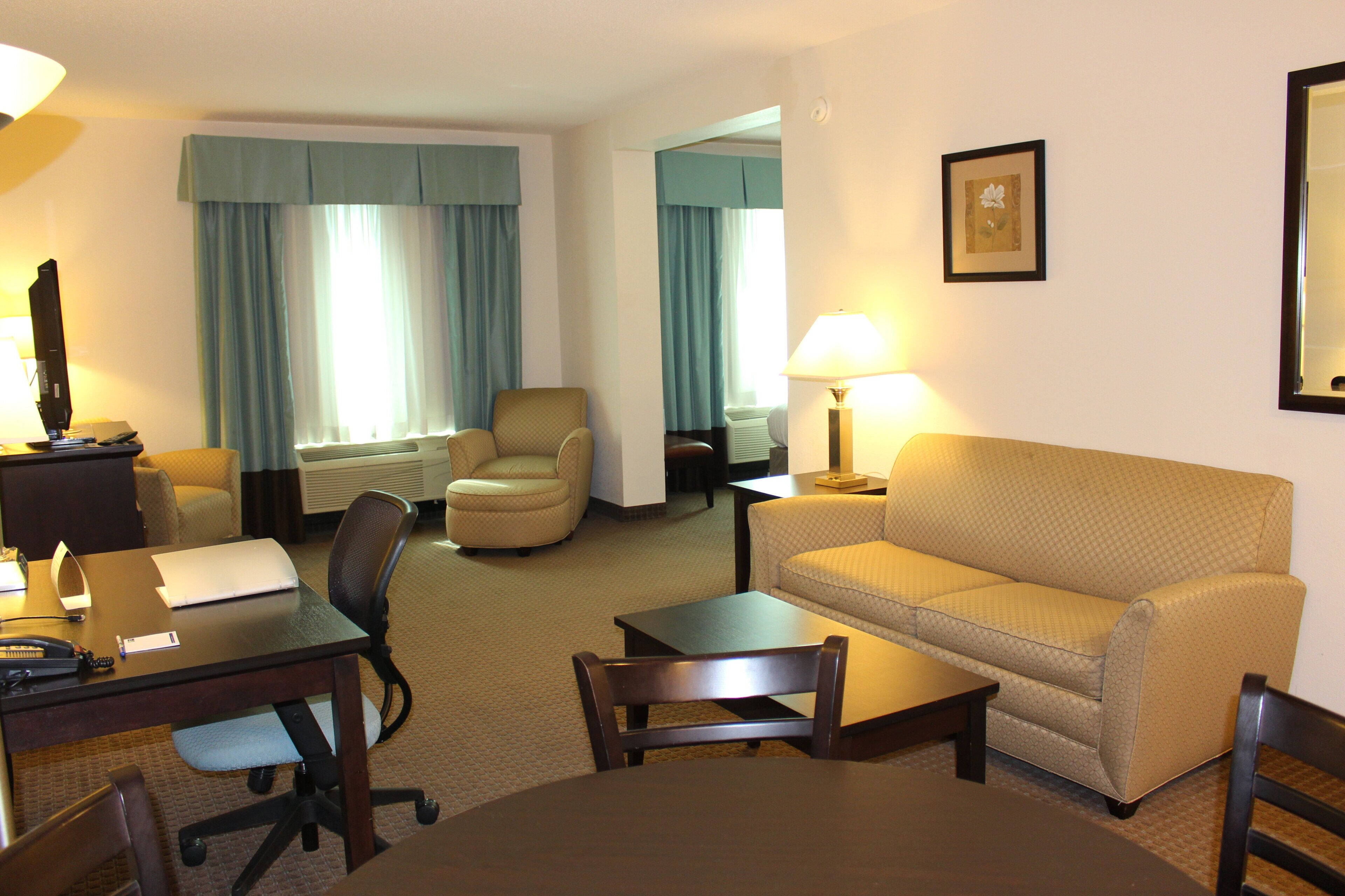 A hotel room with a sofa, two armchairs, a desk with a lamp, a television, and a framed picture on the wall.