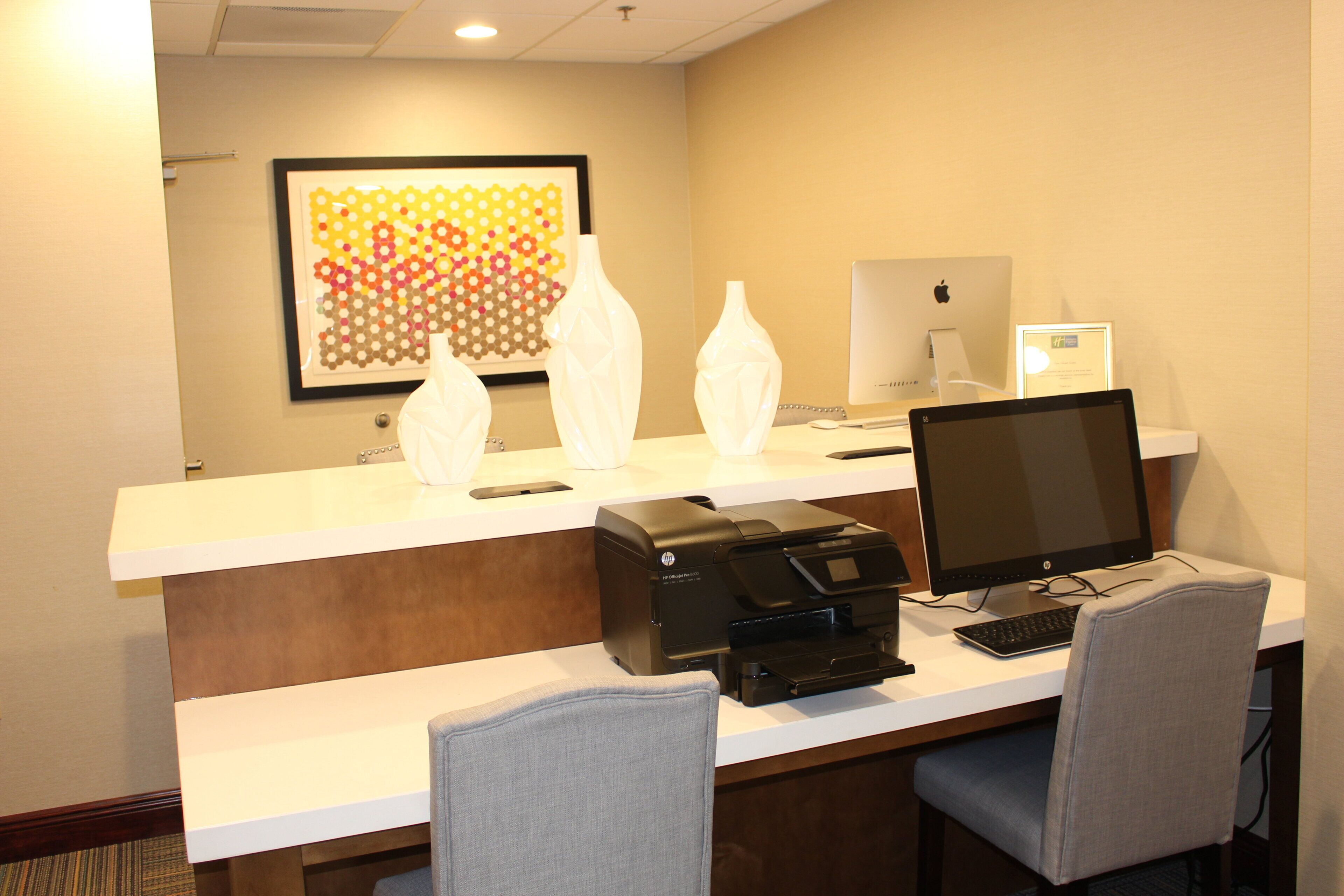 A hotel reception desk with a desktop computer, a printer, and two chairs.