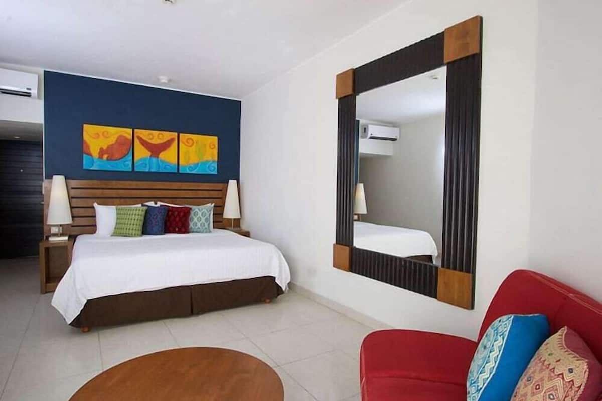 A hotel room with a bed, a red sofa, a round wooden table, and a large mirror.