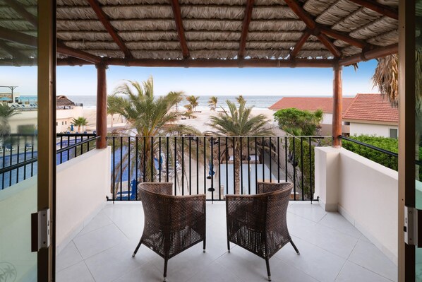 A balcony with wicker chairs, a pool, and a view of the beach and ocean. - Grand Decameron Los Cabos, A Trademark Resort (San José del Cabo)