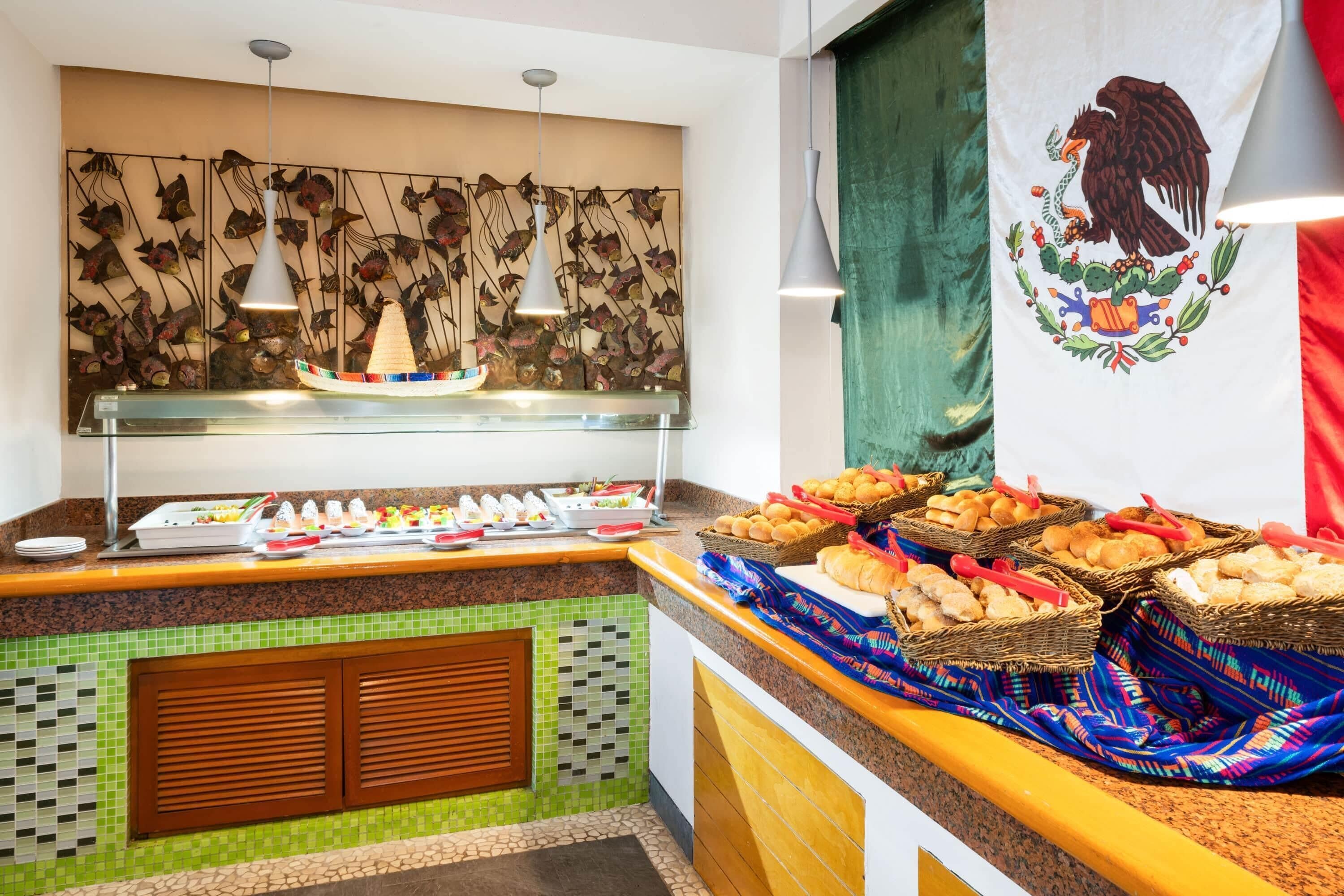 Un bufé con diversos alimentos, una pared decorativa con peces y un bote, y una bandera con un águila.