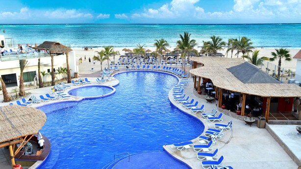 A resort pool with a view of the ocean, surrounded by lounge chairs and palm trees. - Grand Decameron Los Cabos, A Trademark  Resort (San José del Cabo)