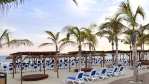 A beach with rows of white lounge chairs and palm trees. - Grand Decameron Los Cabos, A Trademark  Resort (San José del Cabo)