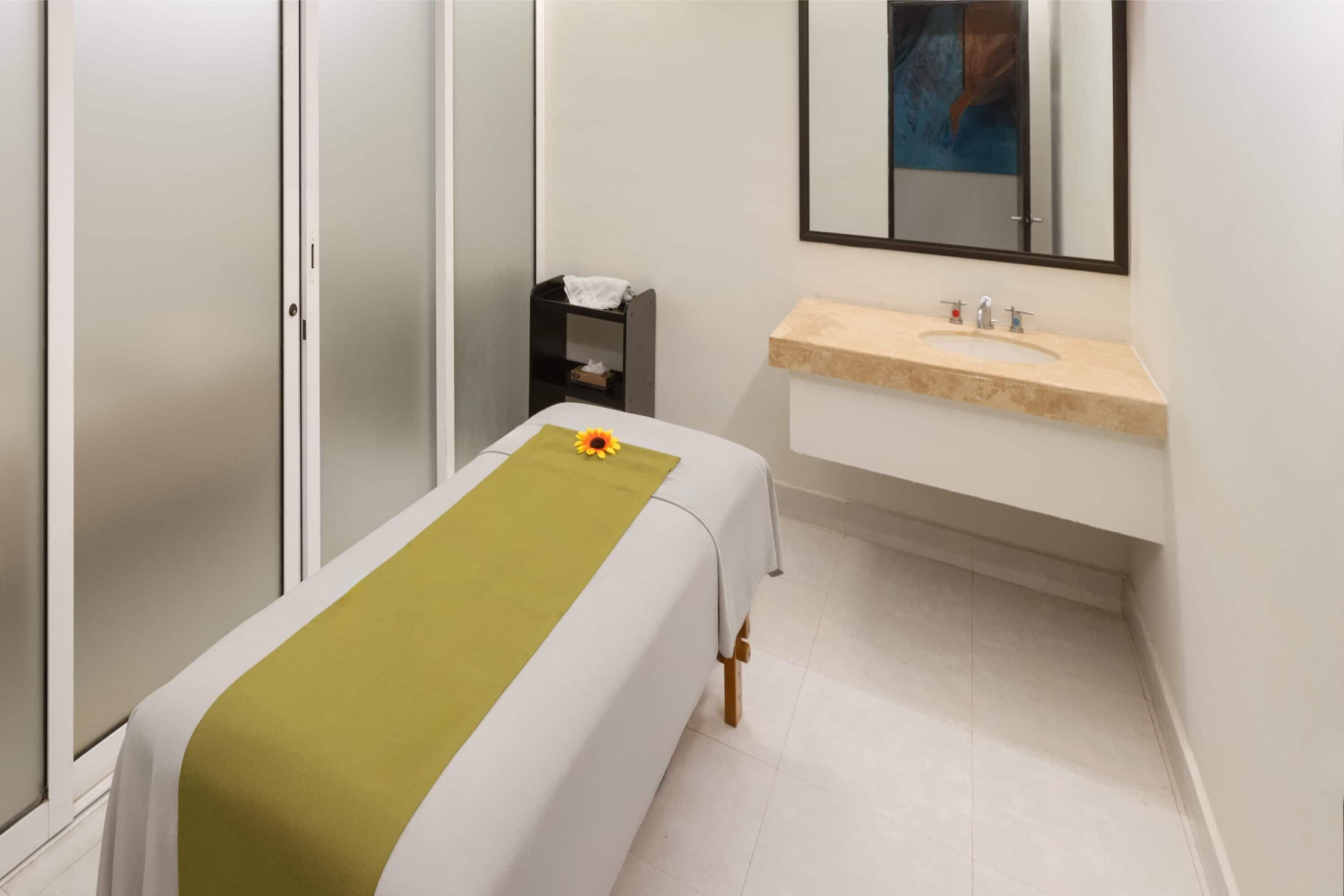A room with a bed, a small bedside table, a mirror, and a sink.