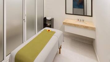 A room with a bed, a small bedside table, a mirror, and a sink.