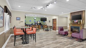 A hotel lobby with a reception desk, a dining area with orange chairs, a fireplace, and a television mounted on the wall. - Best Western Opp Inn (Opp)
